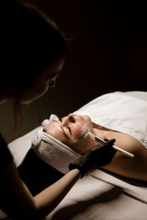 A relaxing spa facial treatment being performed in dramatic low-key lighting.