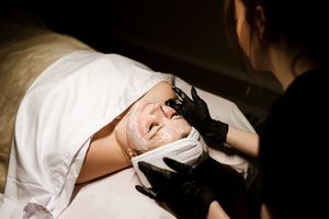 A medical professional wearing black gloves examines a patient lying on a white bed during a medical procedure.