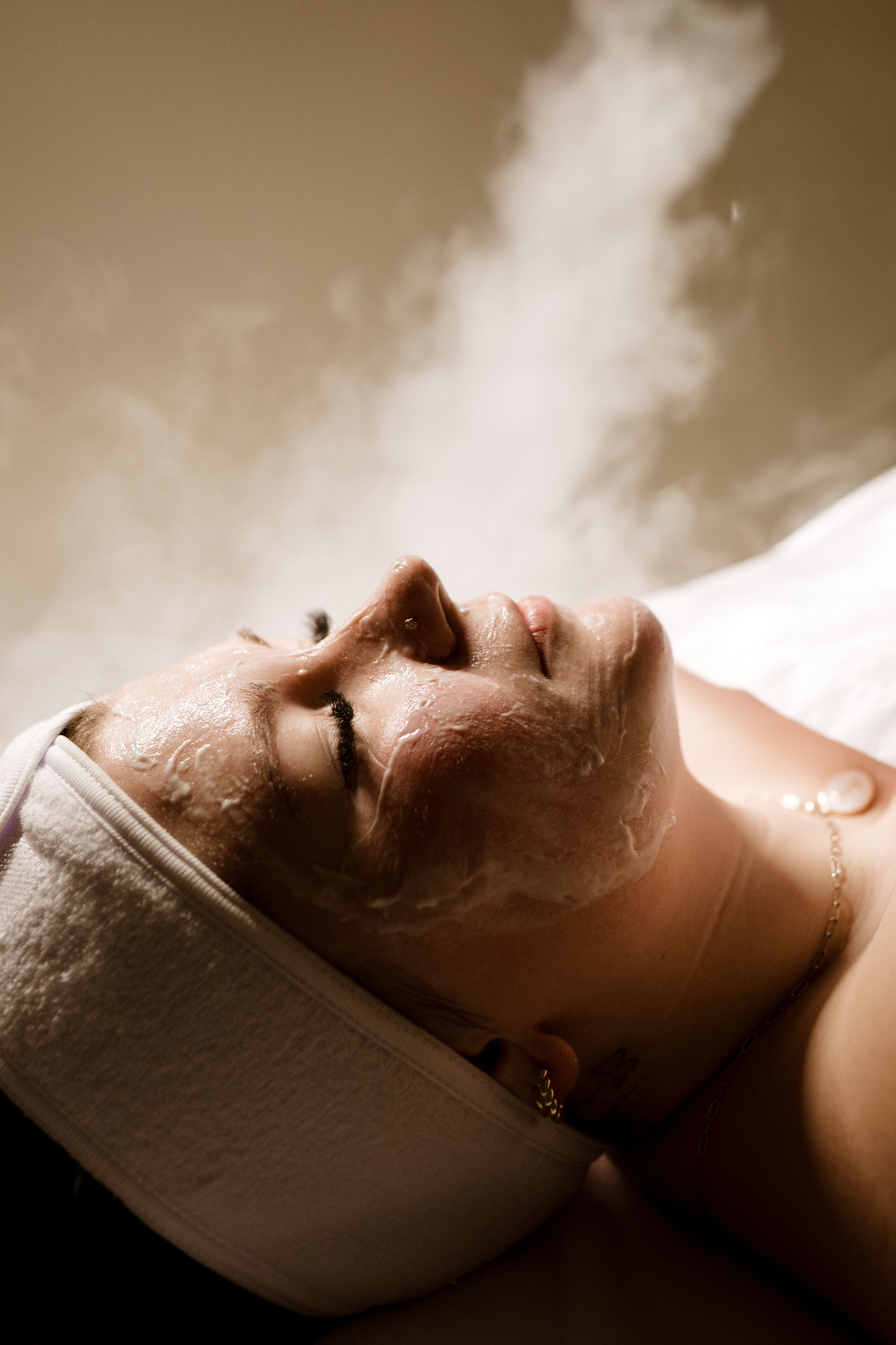 A person relaxes at a spa with a white facial mask treatment in a sepia-toned photograph.