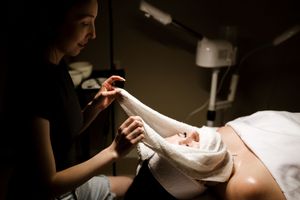 Professional nail technician performing manicure treatment in dimly lit salon setting.