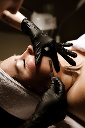Professional beautician wearing black gloves performs facial treatment at luxury spa salon.
