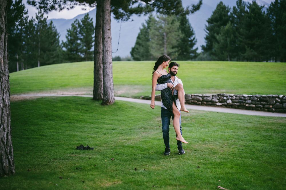 Couple in casual attire posing playfully against a pine tree on a golf course.