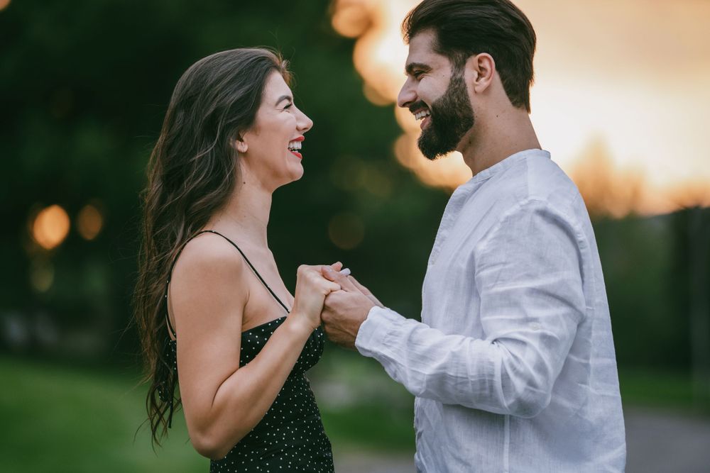 Couple laughs together while holding hands during sunset photoshoot in park.