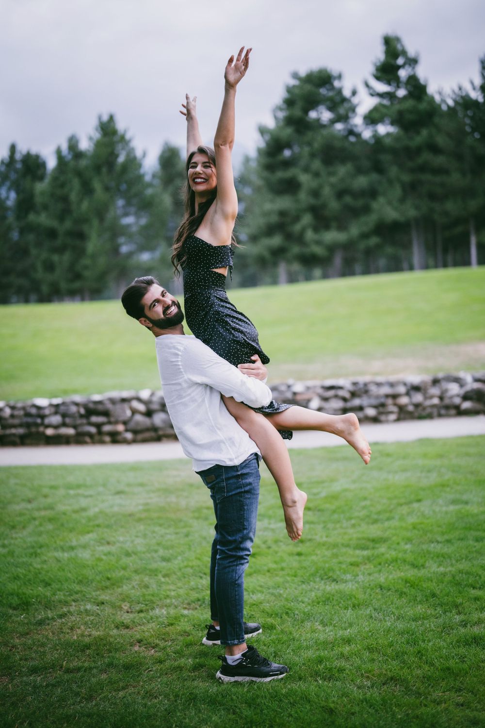 Joyful couple performing a celebratory lift pose on a grassy lawn.