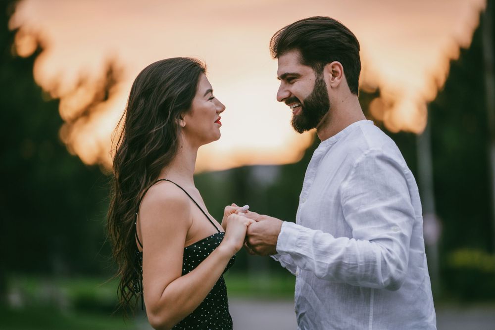Couple holds hands while sharing romantic moment at sunset in park setting.