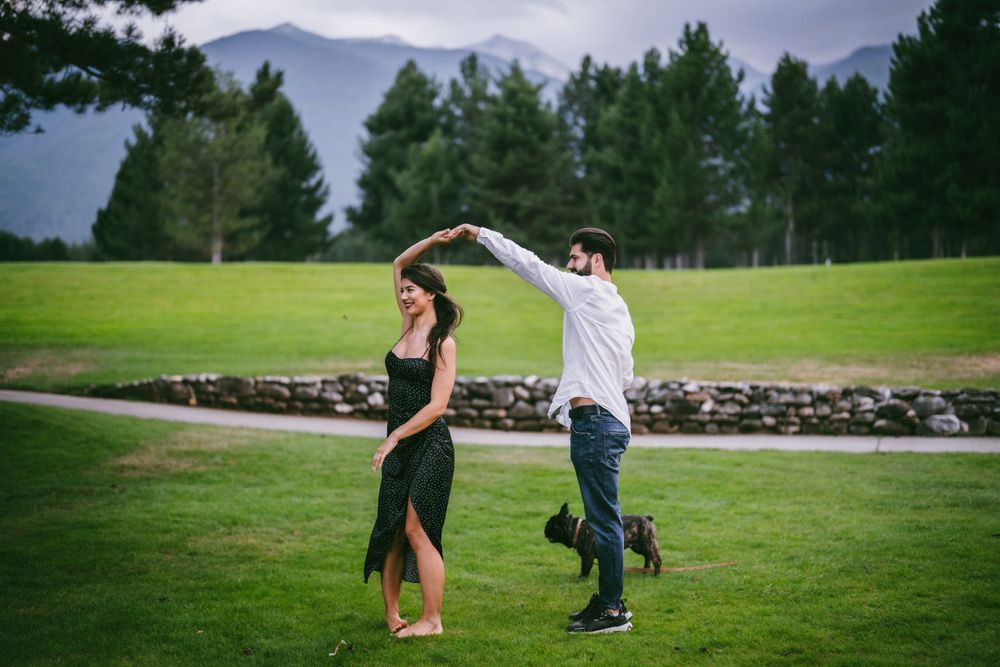 Couple dancing playfully on a green lawn with mountains in the background.
