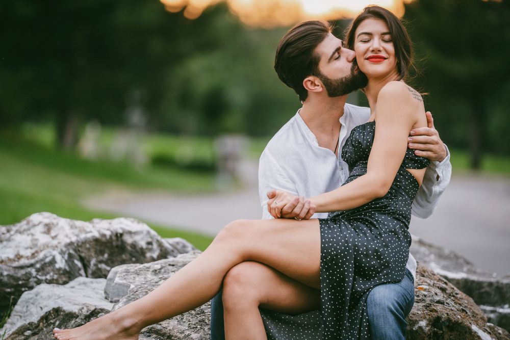 Affectionate couple in polka dot dress and white shirt embrace on rocky landscape.