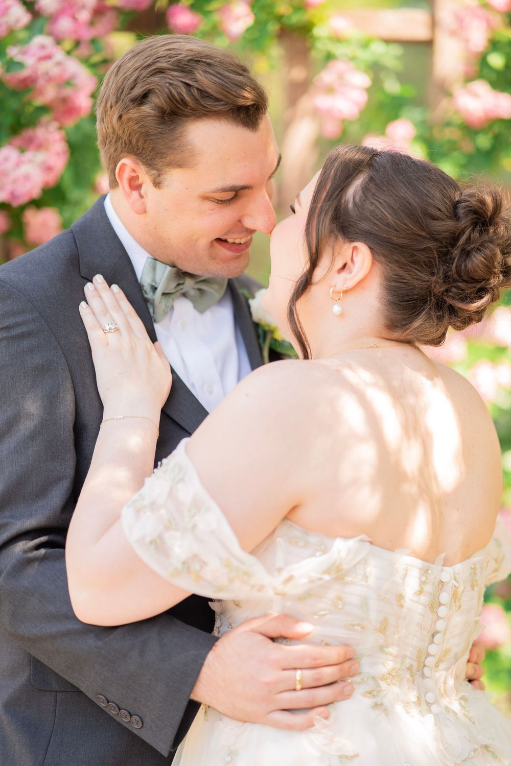 Bride and groom sharing a romantic moment, nearly kissing, surrounded by pink blossoms.