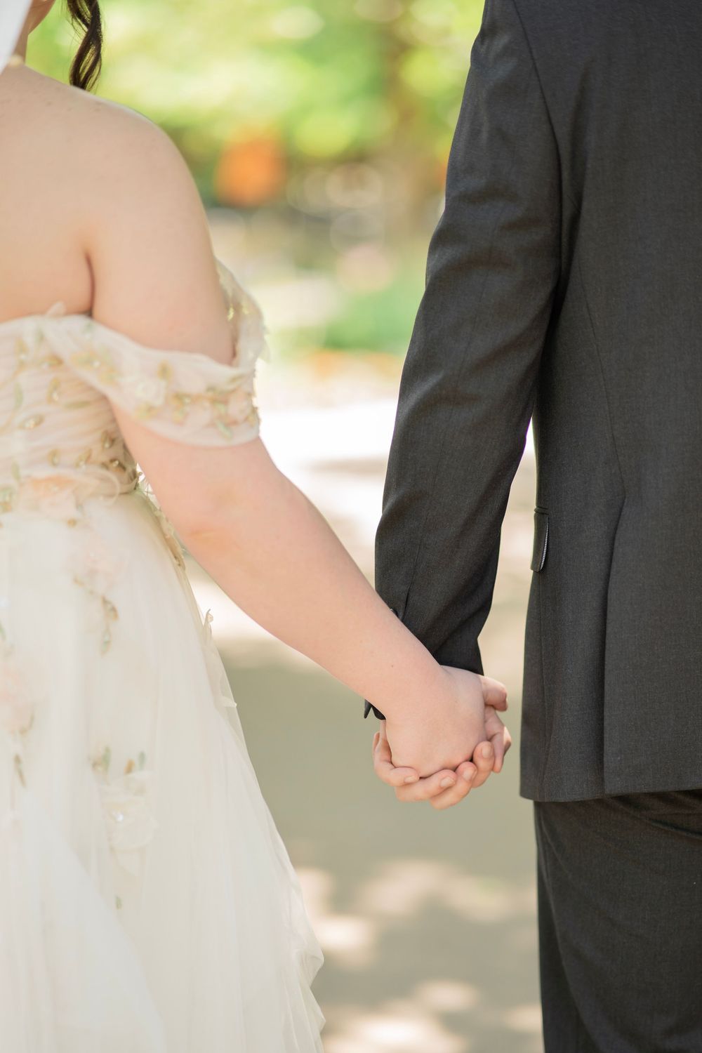 Close-up of bride and groom holding hands while walking together on their wedding day.