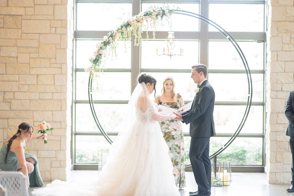 Bride and groom exchange vows under a circular floral arch with chandelier in elegant venue.