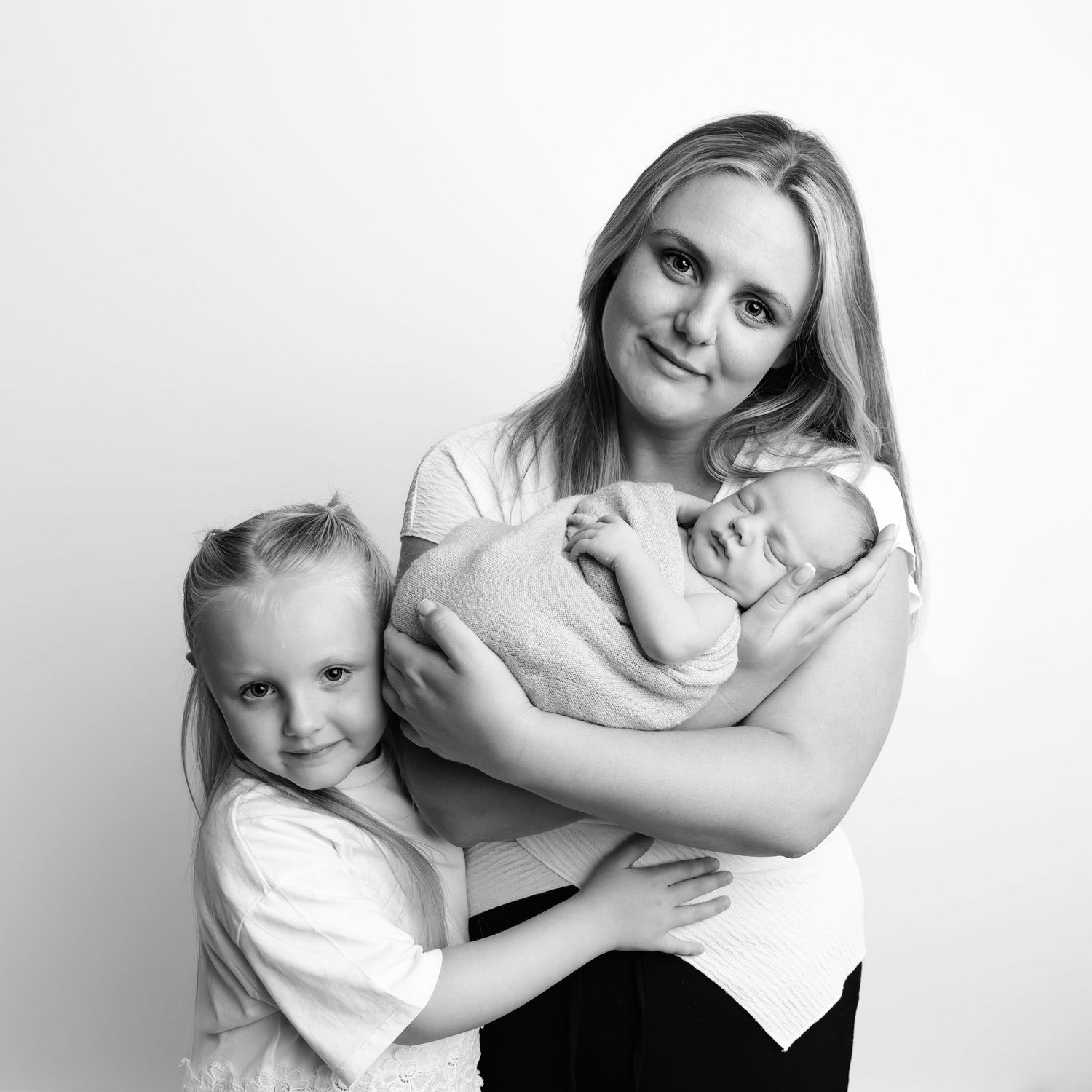 Black & White image of Mum holding her newborn baby smiling and her little girl aged 7 also cuddling baby. Taken in my studio in Coventry