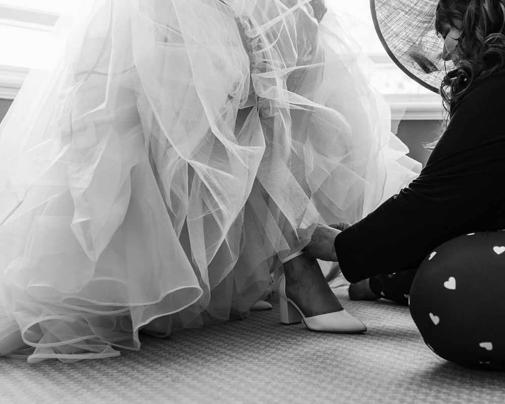 Black and white image of someone adjusting the layers of a white wedding dress on the floor.