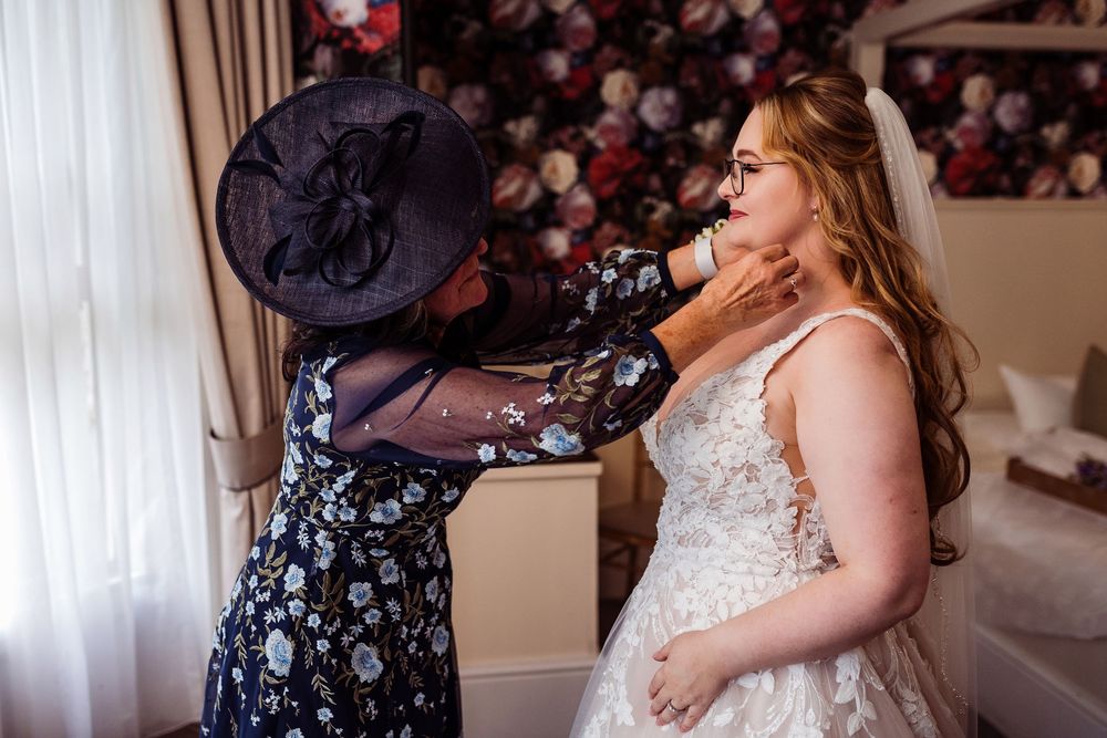 A bride and bridesmaid share a tender embrace during an emotional wedding day moment.