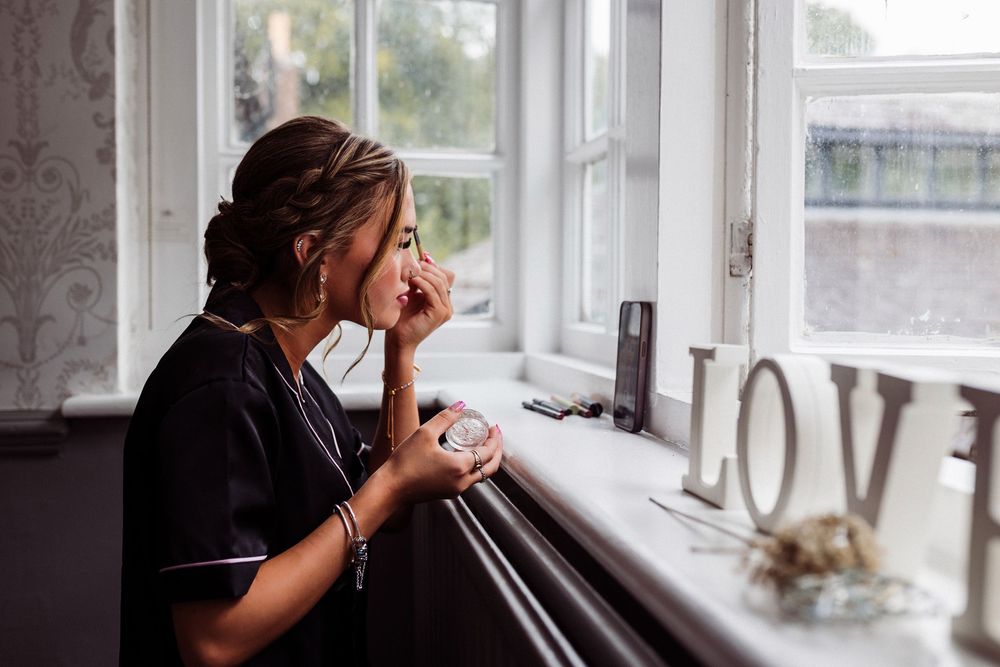 Person sitting by window sill holding white coffee mug in moody natural lighting.