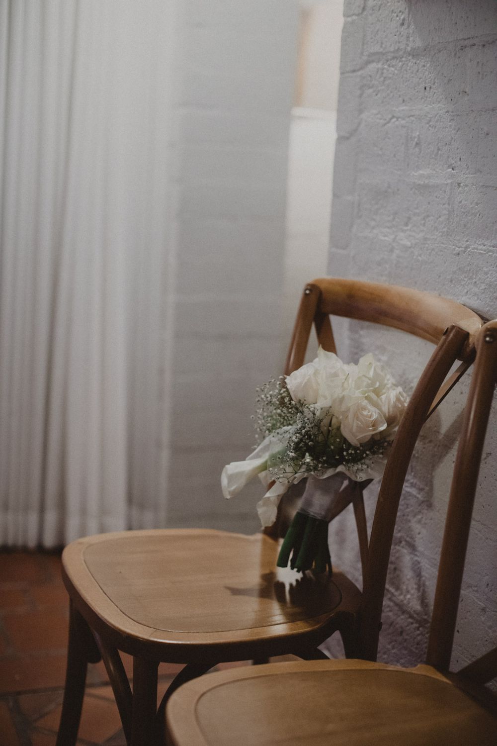 Wooden chairs with white floral arrangements sit against a light gray wall in a minimalist setting.