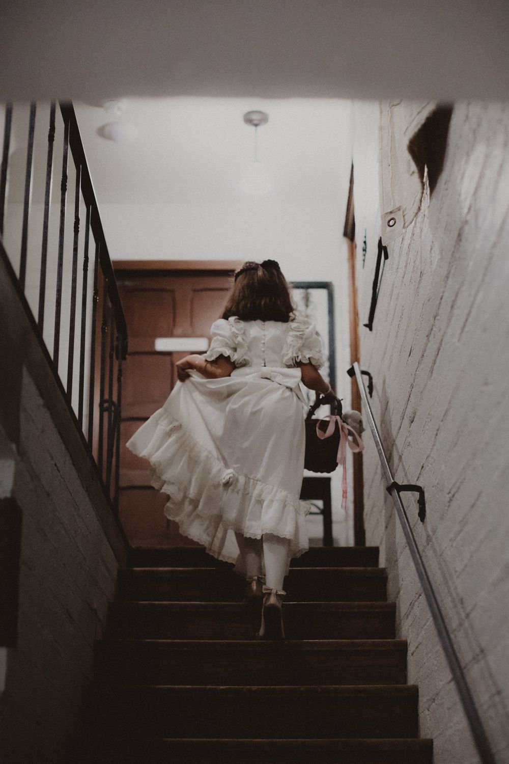 A flowing white wedding dress captured in motion while ascending a dimly lit staircase.