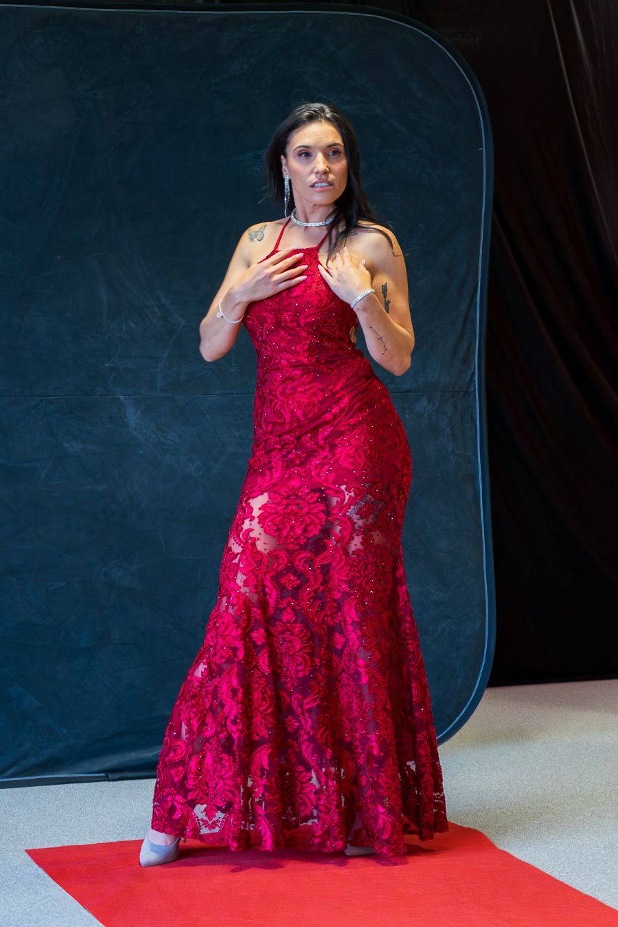 Model twirls in a flowing red lace dress during a fashion photoshoot on a dark set.