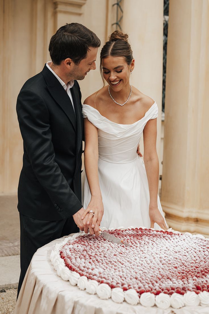 Smiling bride and groom cutting a large round cake decorated with red berries.