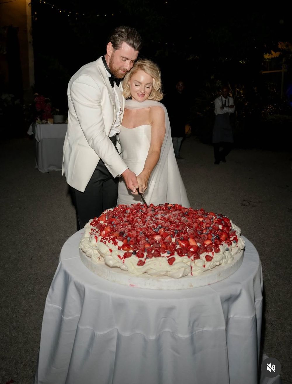 Bride and groom cutting a large strawberry wedding cake outdoors at night.