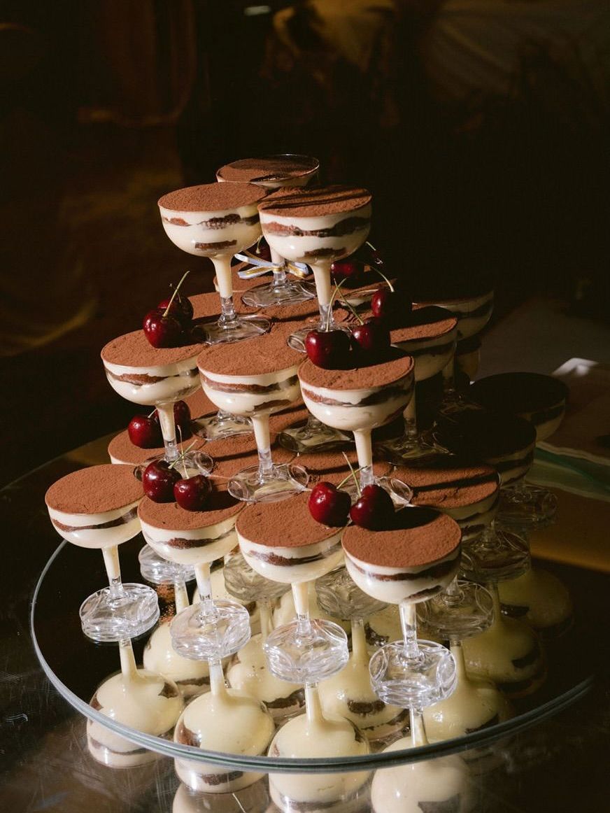Elegant tiered display of tiramisu desserts in glasses topped with cherries.