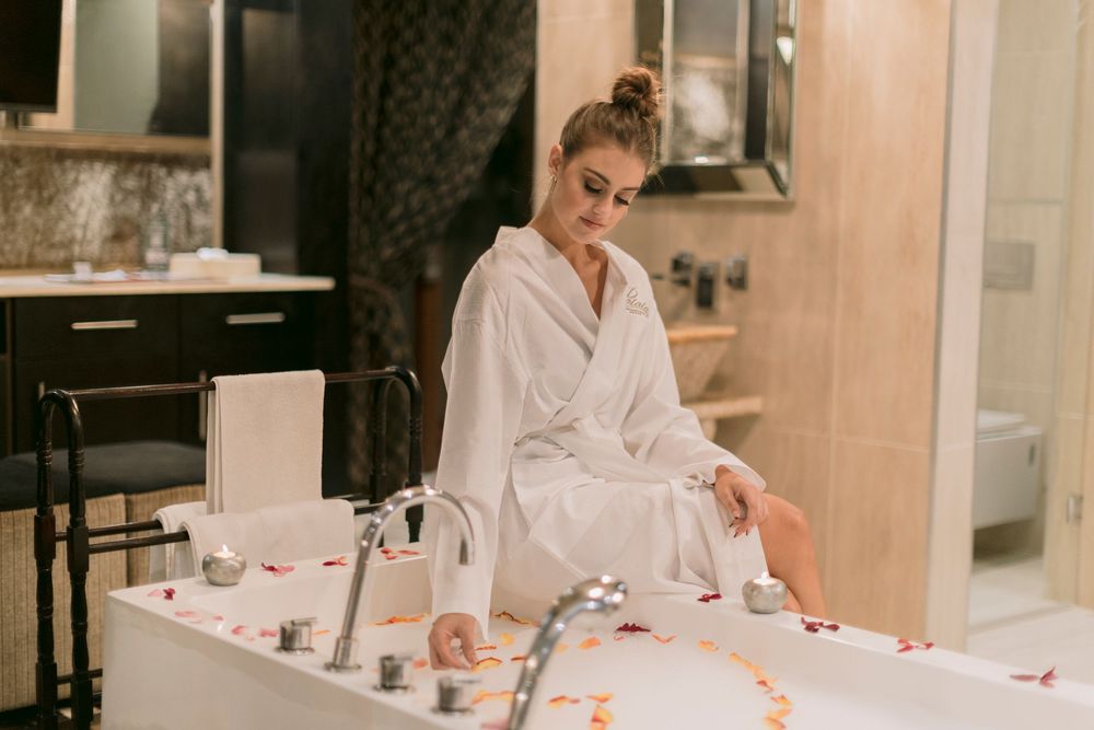 Woman in white robe preparing a luxurious flower petal bath in elegant hotel bathroom.