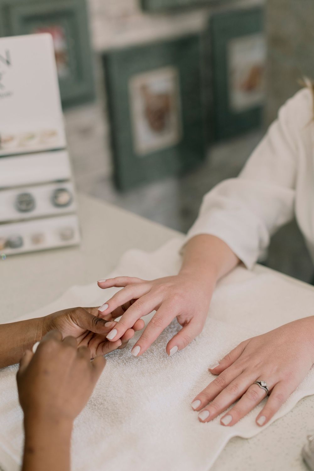 Close-up of nail technician buffing client's nails on white towel at beauty salon.