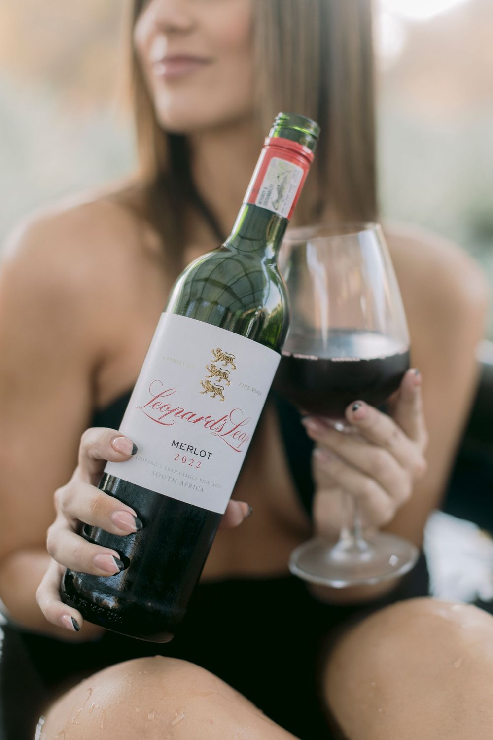 Woman holding Leopards Leap Merlot wine bottle and glass of red wine outdoors.