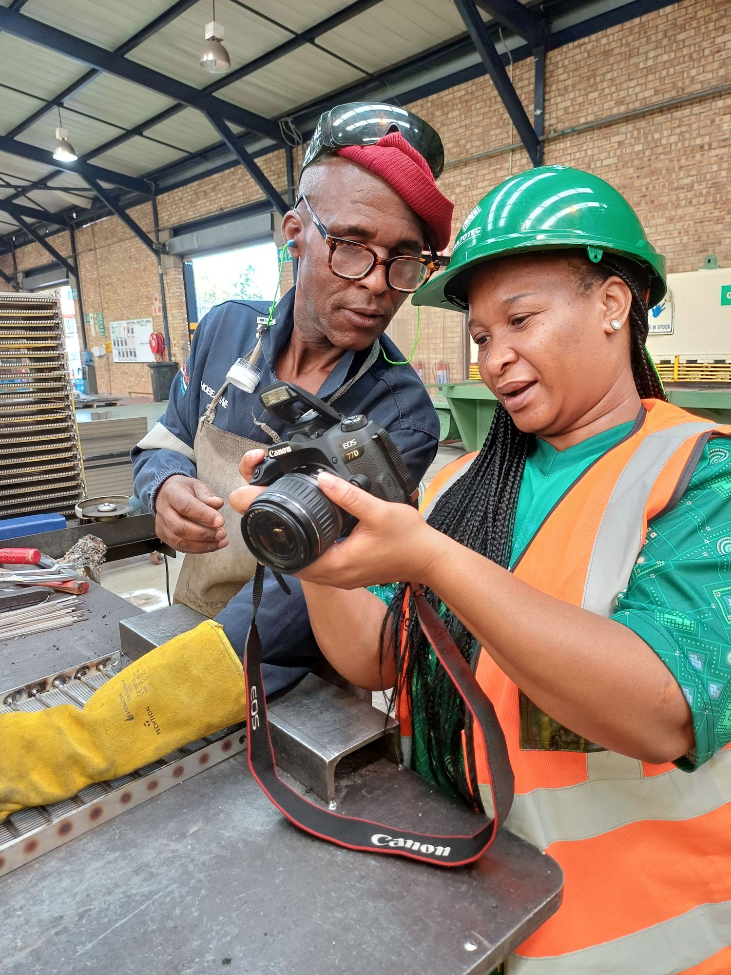 Photography student reviewing a freshly taken commercial image with her subject, learning professional techniques in a factory setting.