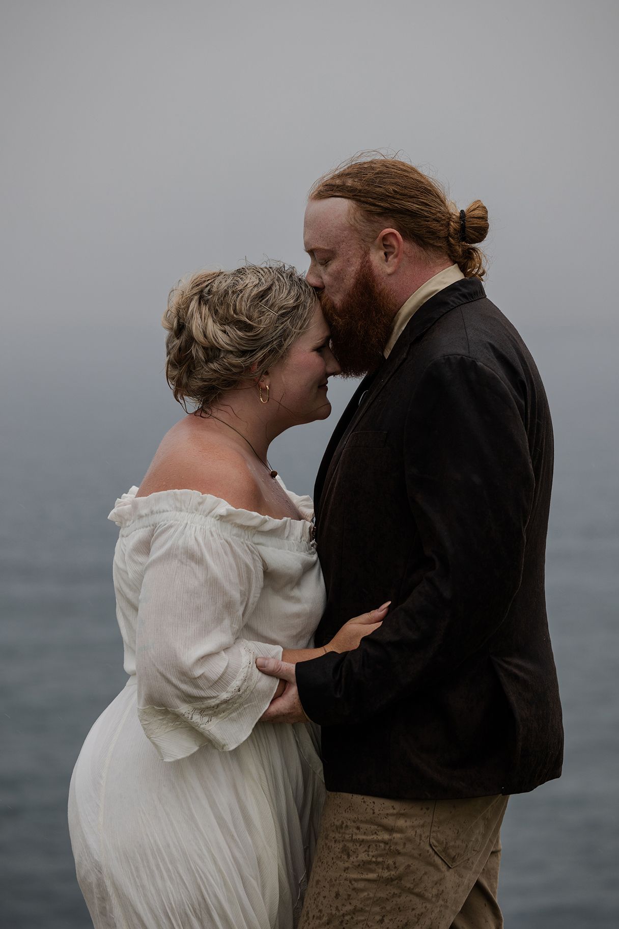 Newlyweds sharing a quiet moment under dark coastal skies during Ireland adventure elopement