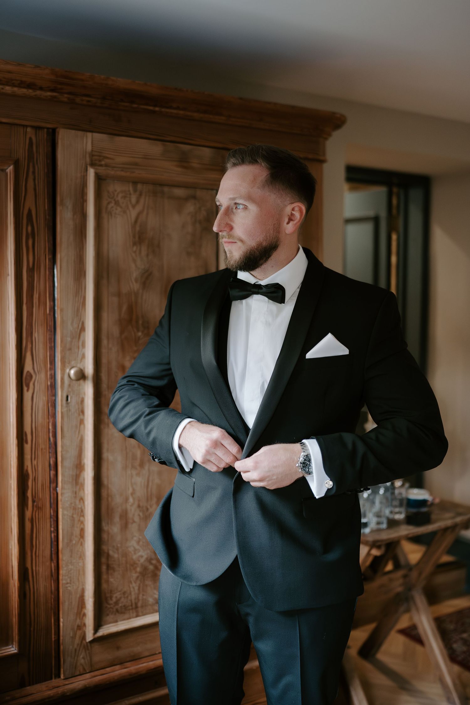 groom fastening tux jacket button at ivy lodge in cirencester