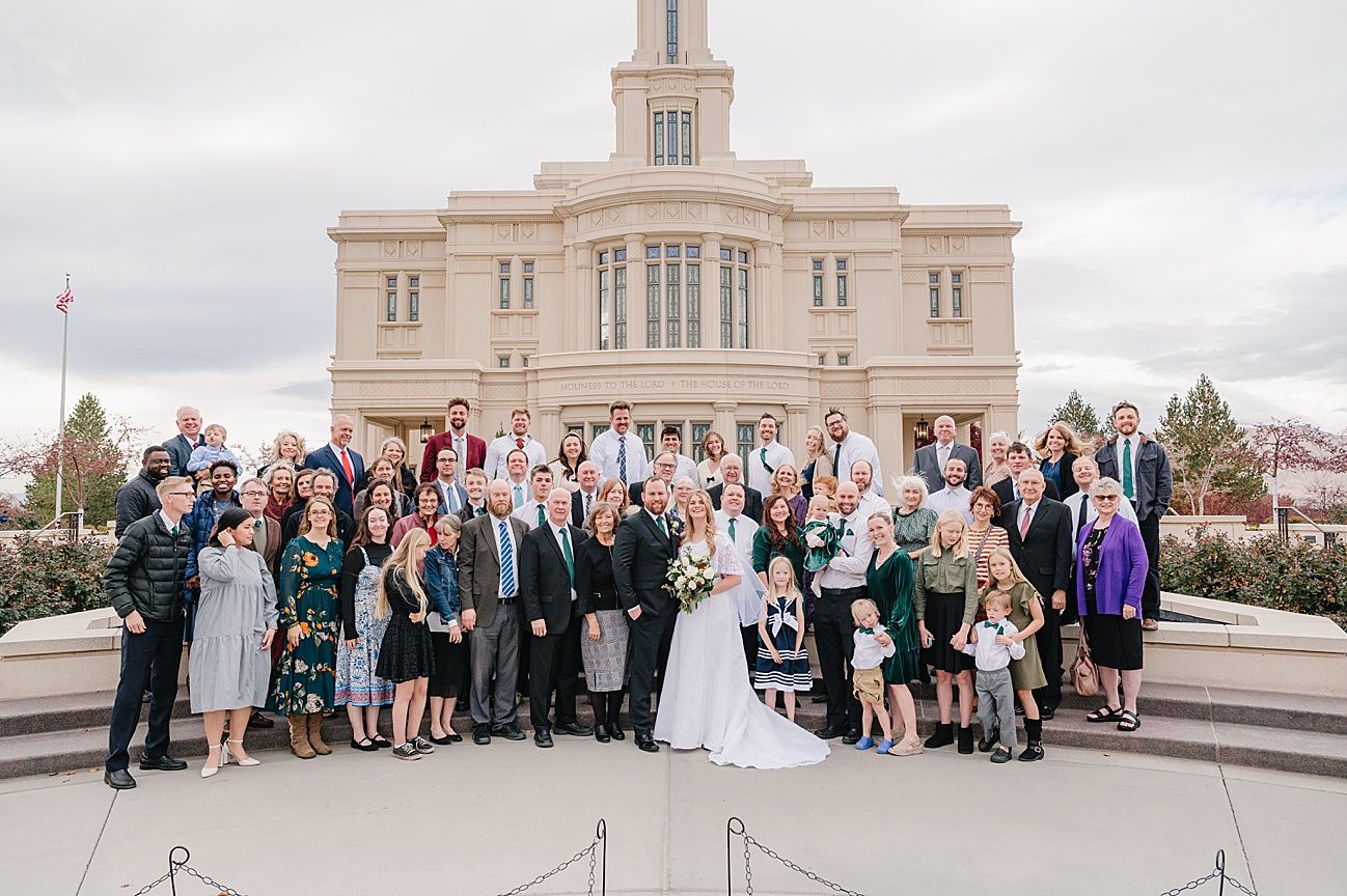 A large wedding party poses together on the steps of an elegant temple building with a tower spire.