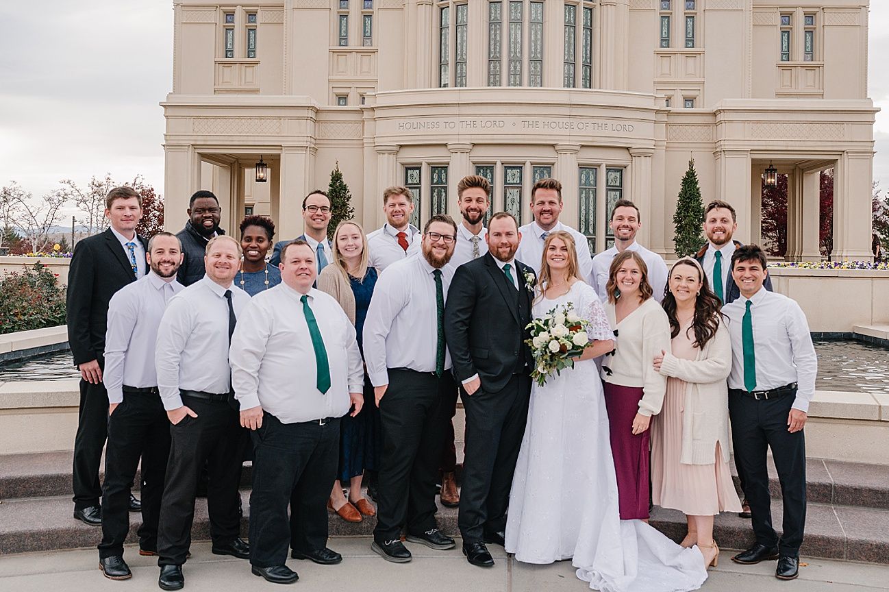 Wedding party poses on grand stone steps of elegant building in formal attire with white and teal color scheme.