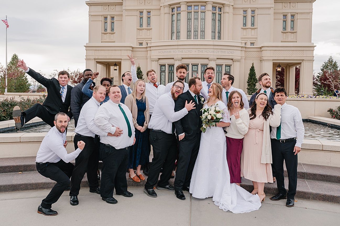 Wedding party poses playfully on stone steps outside a classical building during photo session.