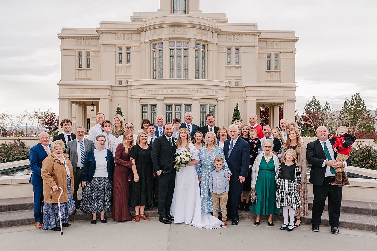 Wedding party members gather on the steps of a grand stone building for formal group photos.