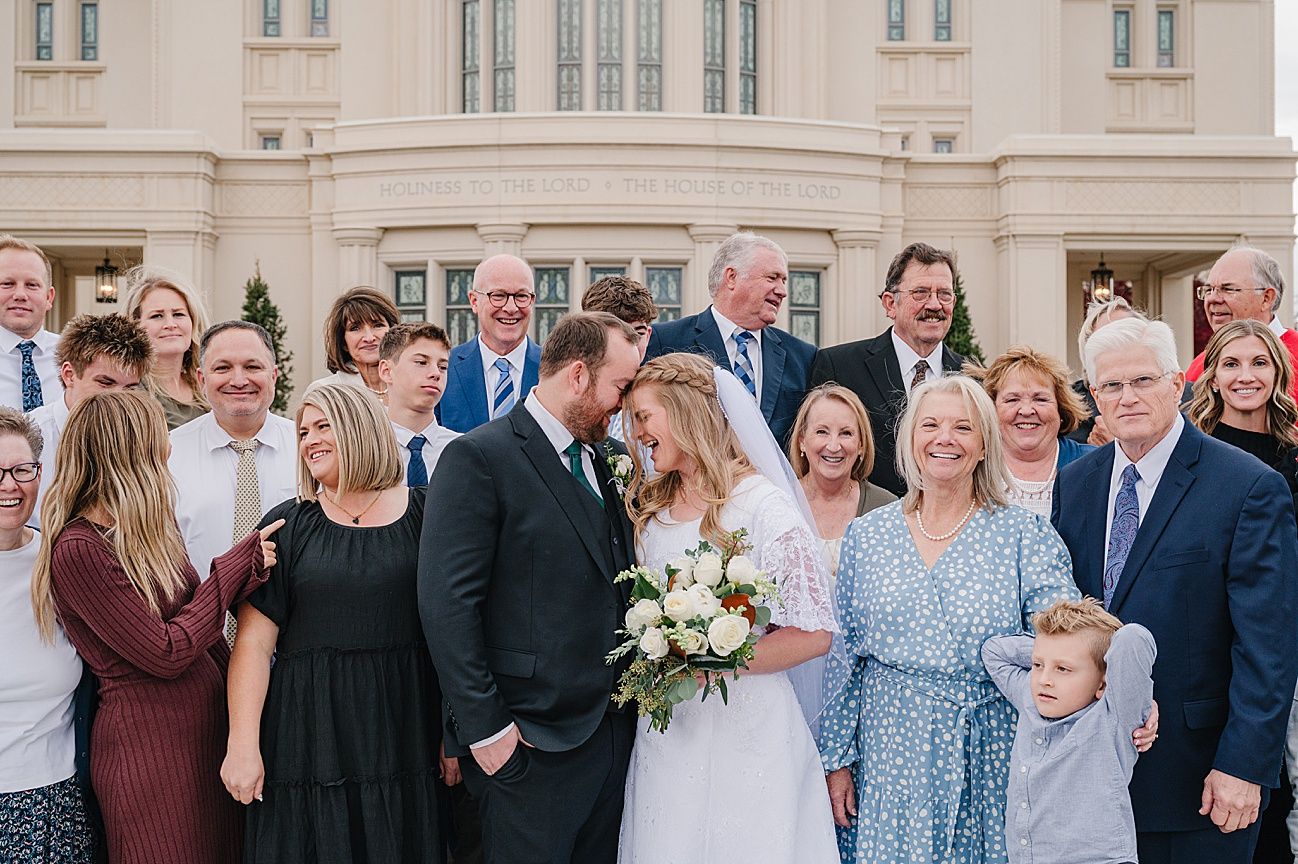 Wedding party guests smile and celebrate together outside a light colored building.