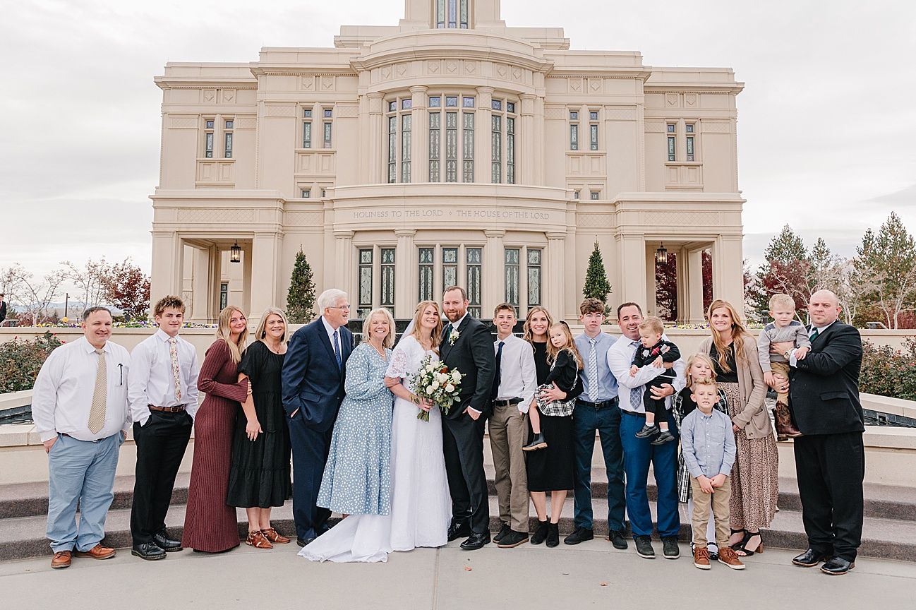 Large family group gathered on steps of ornate stone building for formal wedding photos.