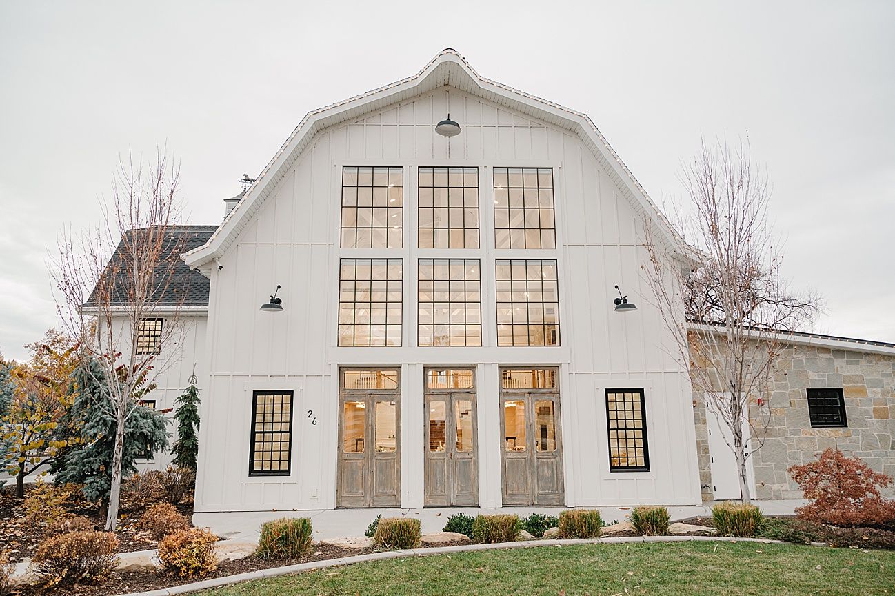 A modern white barn-style event venue with large windows and elegant architectural details against an overcast sky.