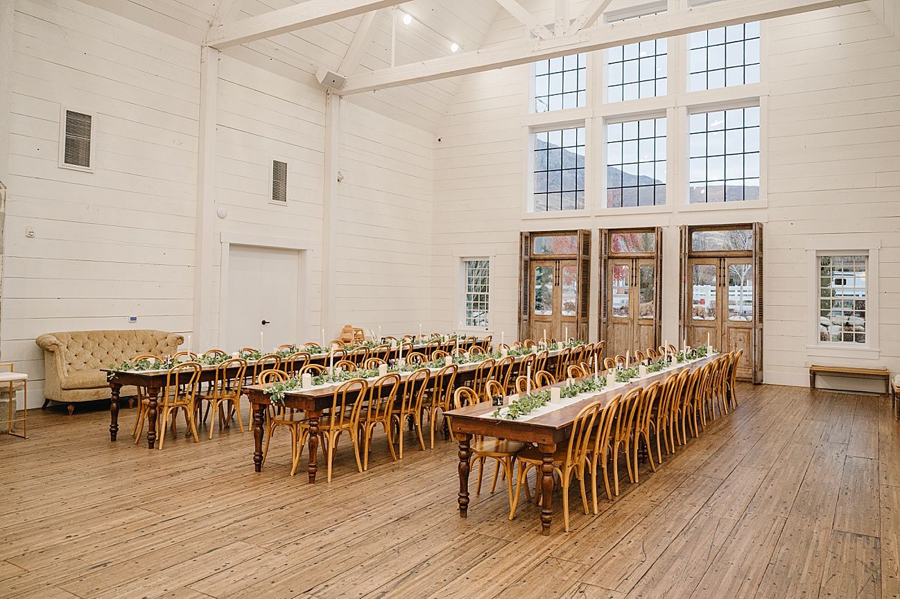 Long white reception hall with wooden tables and chairs arranged in rows beneath industrial windows.