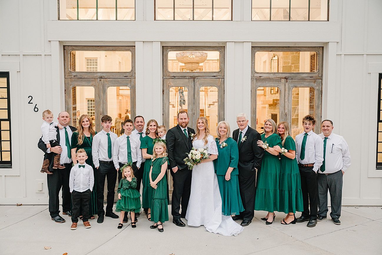 Panoramic view of wedding party posing together against white building exterior with windows.