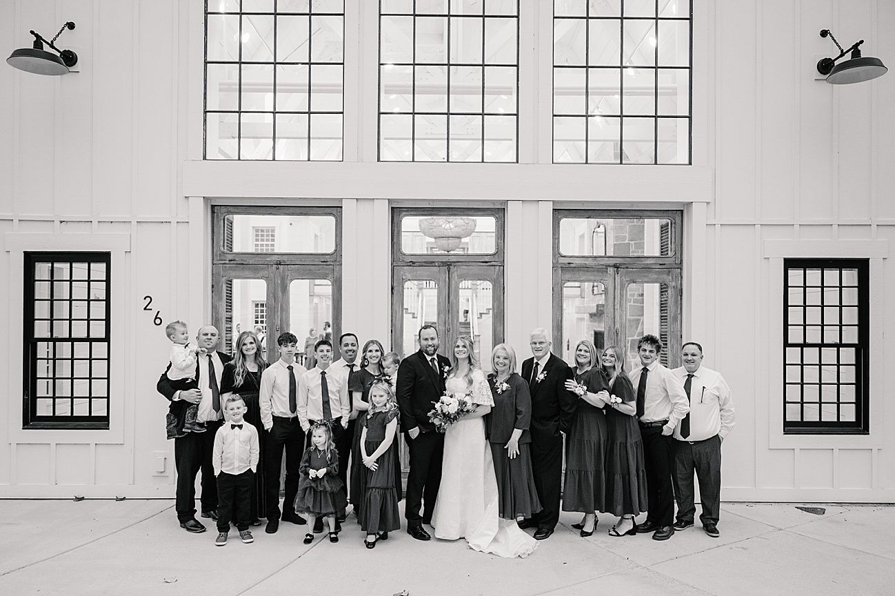 Wedding party lined up against white church wall with large windows in formal attire.