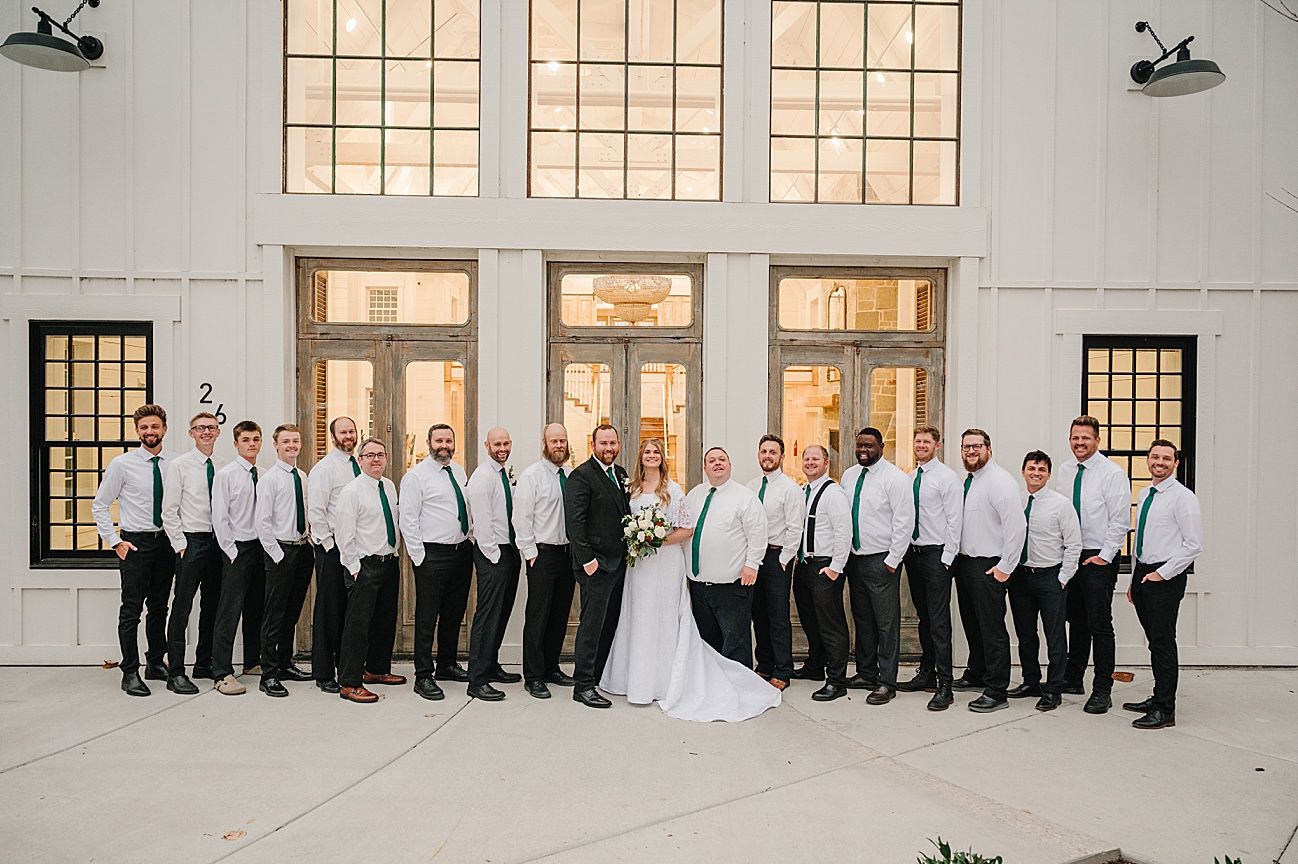 Large wedding party poses in front of church windows in black and white formal attire.