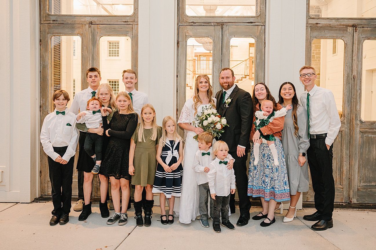 Large group portrait of wedding guests lined up against a light colored wall in an elegant venue.