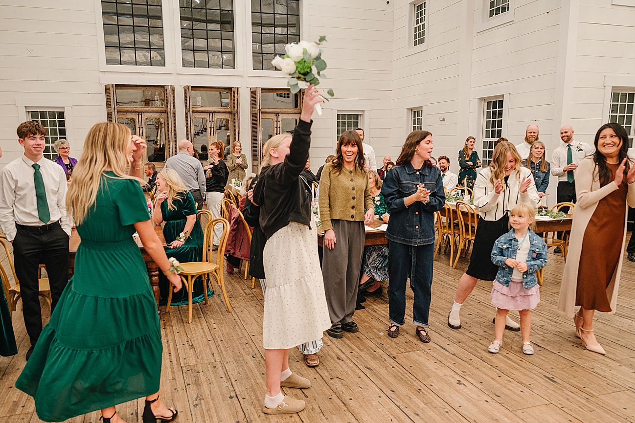 Wedding party dances and celebrates on a rustic wooden floor during a lively reception.