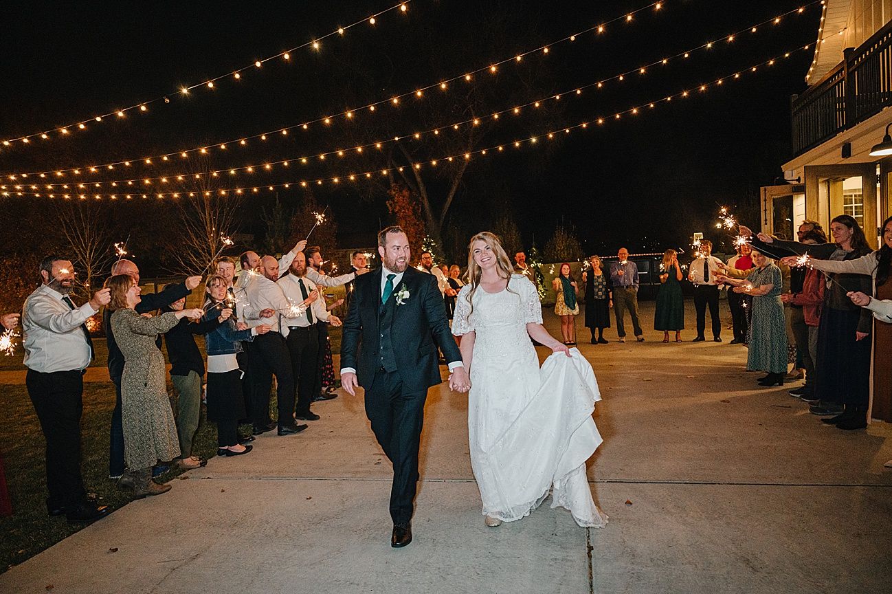 Wedding guests dance and celebrate under romantic string lights at an outdoor evening reception.