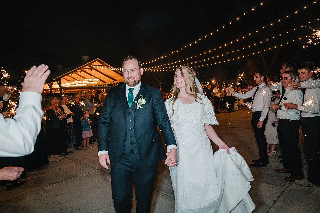 Wedding guests dance and celebrate under twinkling string lights at an outdoor evening reception.