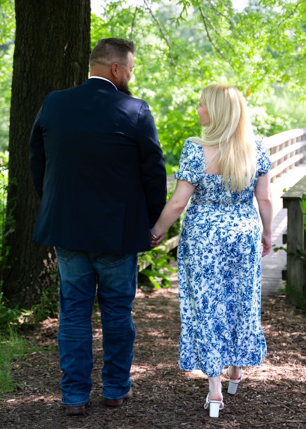 A couple walking through a wooded path wearing blue and navy casual attire.