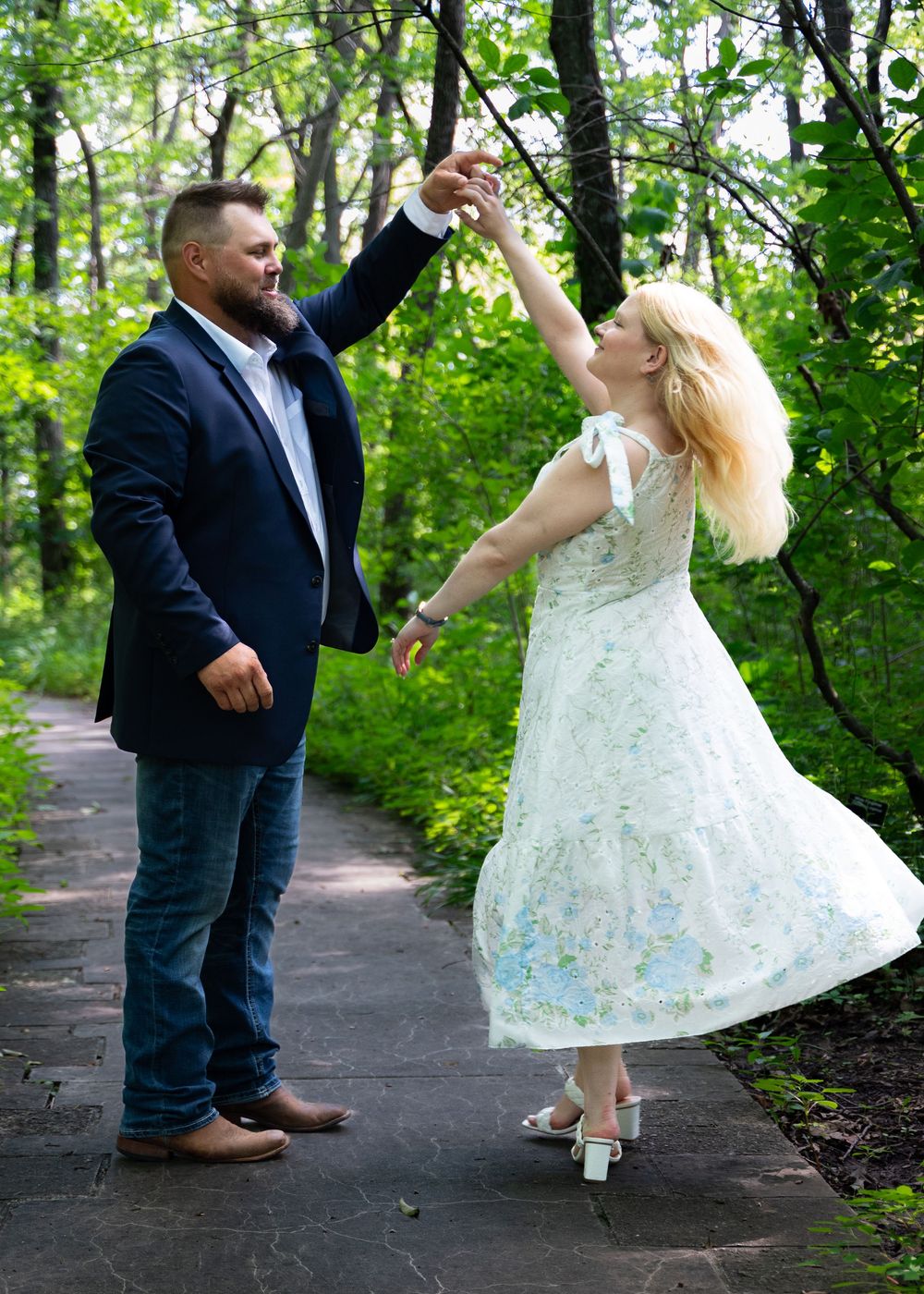 Couple dancing joyfully on a woodland path with the bride wearing a vintage-style white dress.