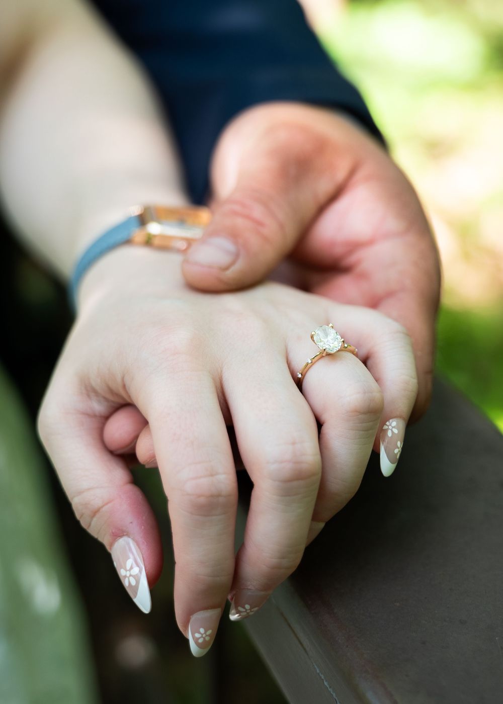 Close-up of hands displaying engagement ring and delicate manicure against natural lighting.