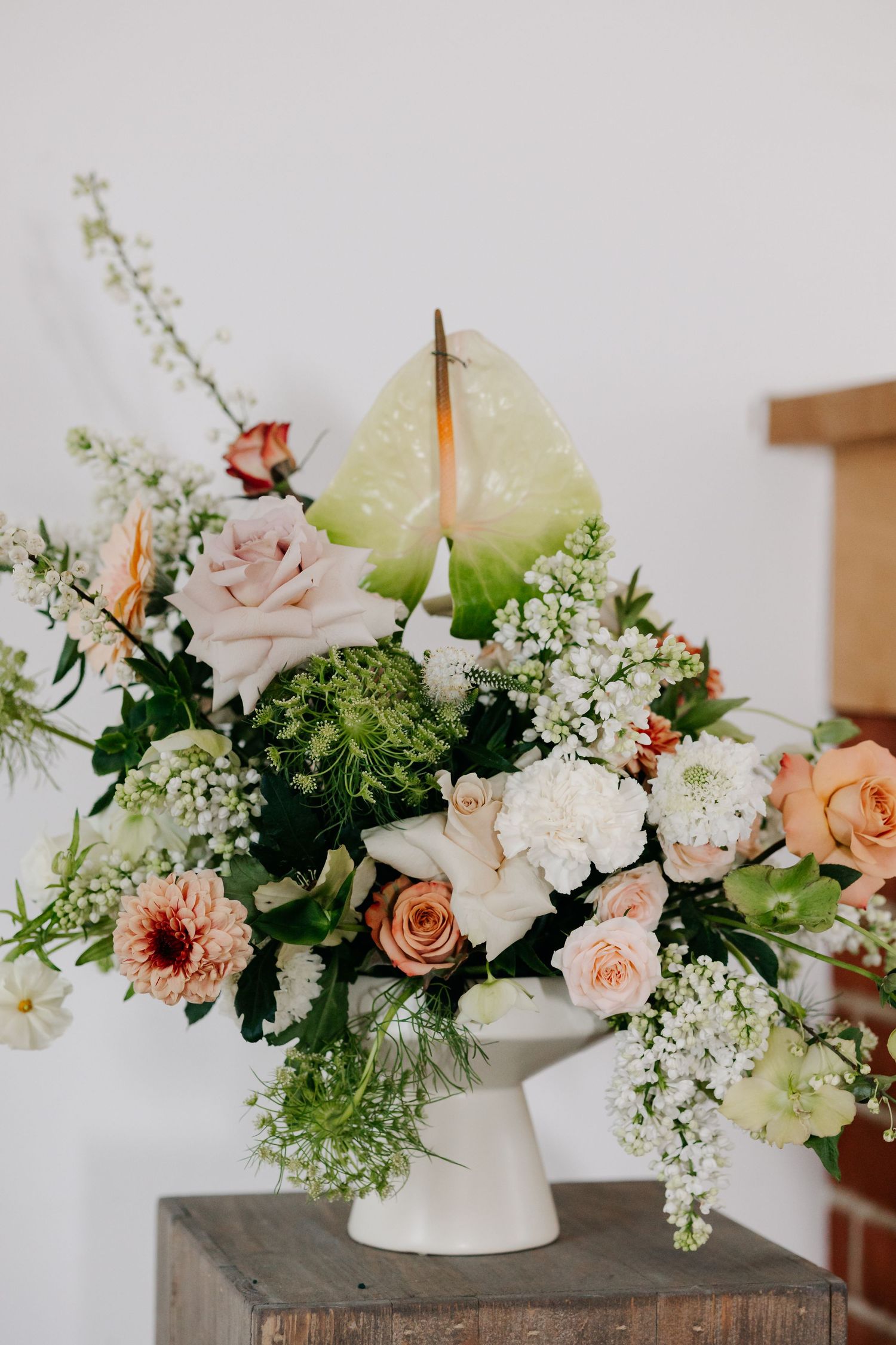 A romantic floral arrangement with peach roses, white delphinium, and greenery displayed on a rustic surface. product photography