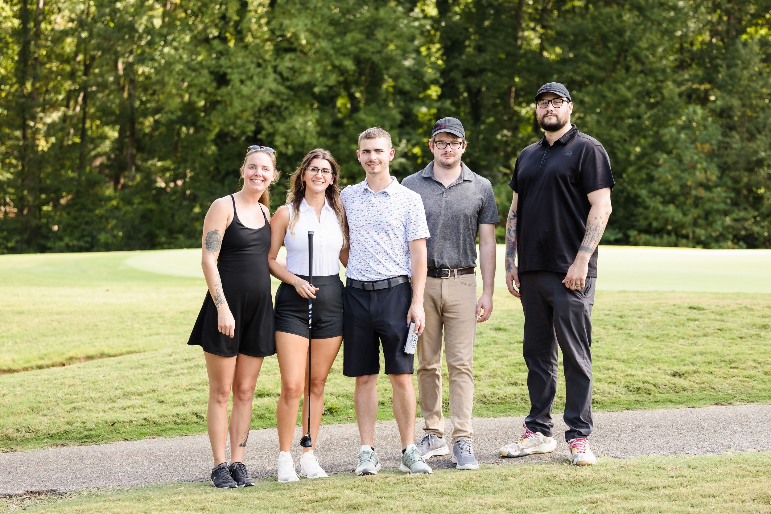 Group of people standing together outdoors on a sunny day near walking path.